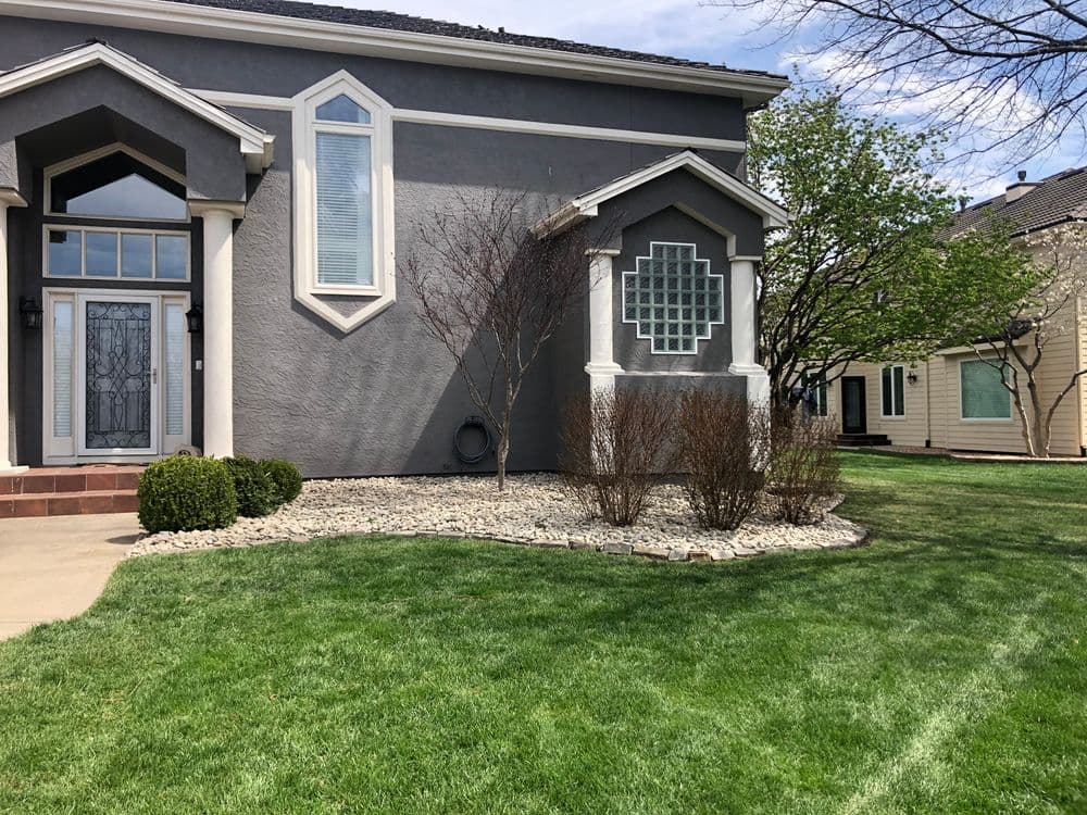 Modern gray house with landscaped yard, featuring decorative stone and mature trees.