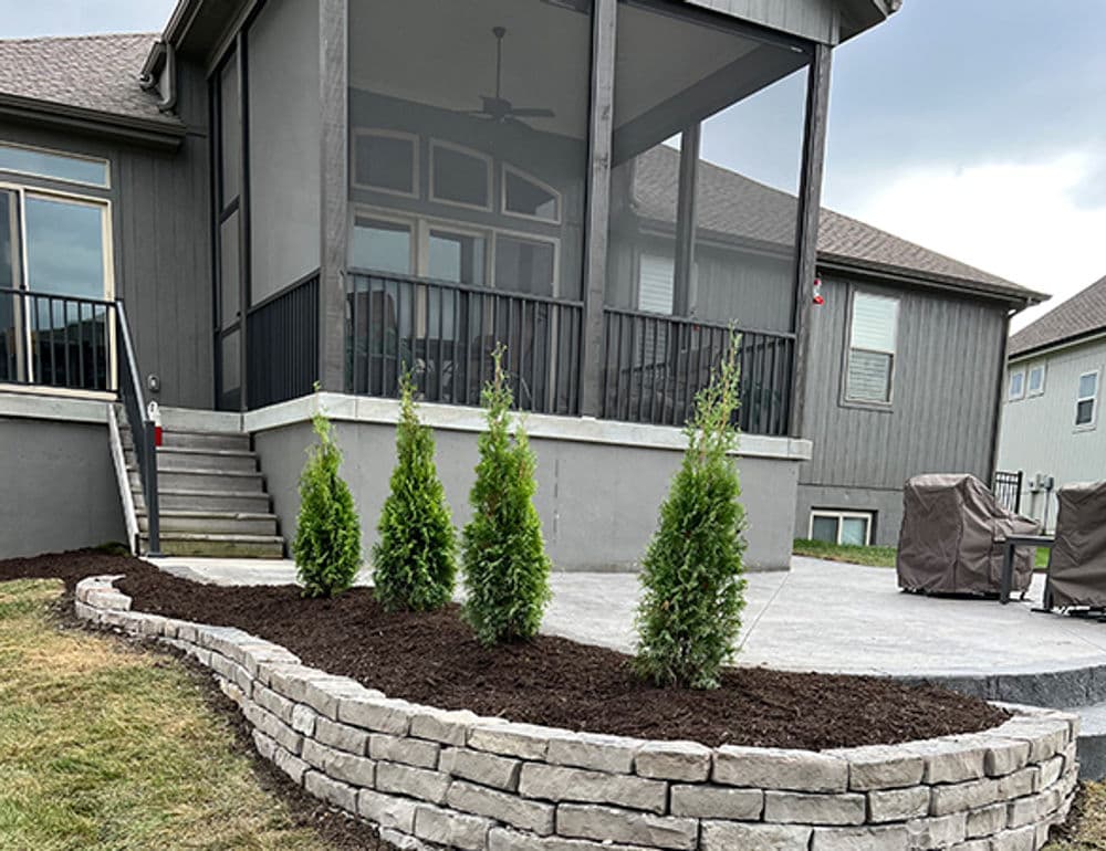 Modern home exterior with a screened porch, stone landscaping, and neatly trimmed evergreen shrubs.