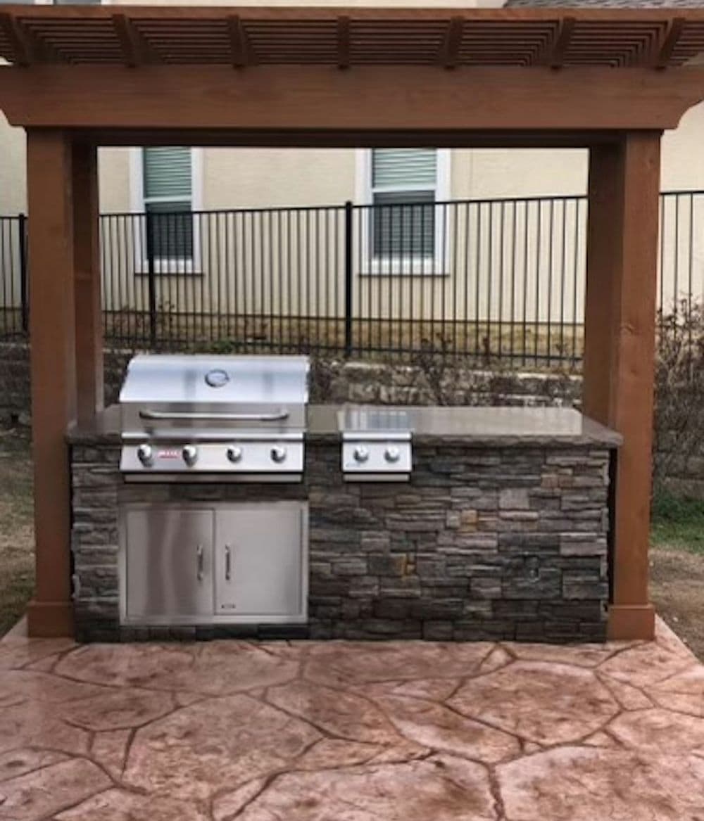 Outdoor kitchen with a stone grill station under a wooden pergola. Stylish and modern design.
