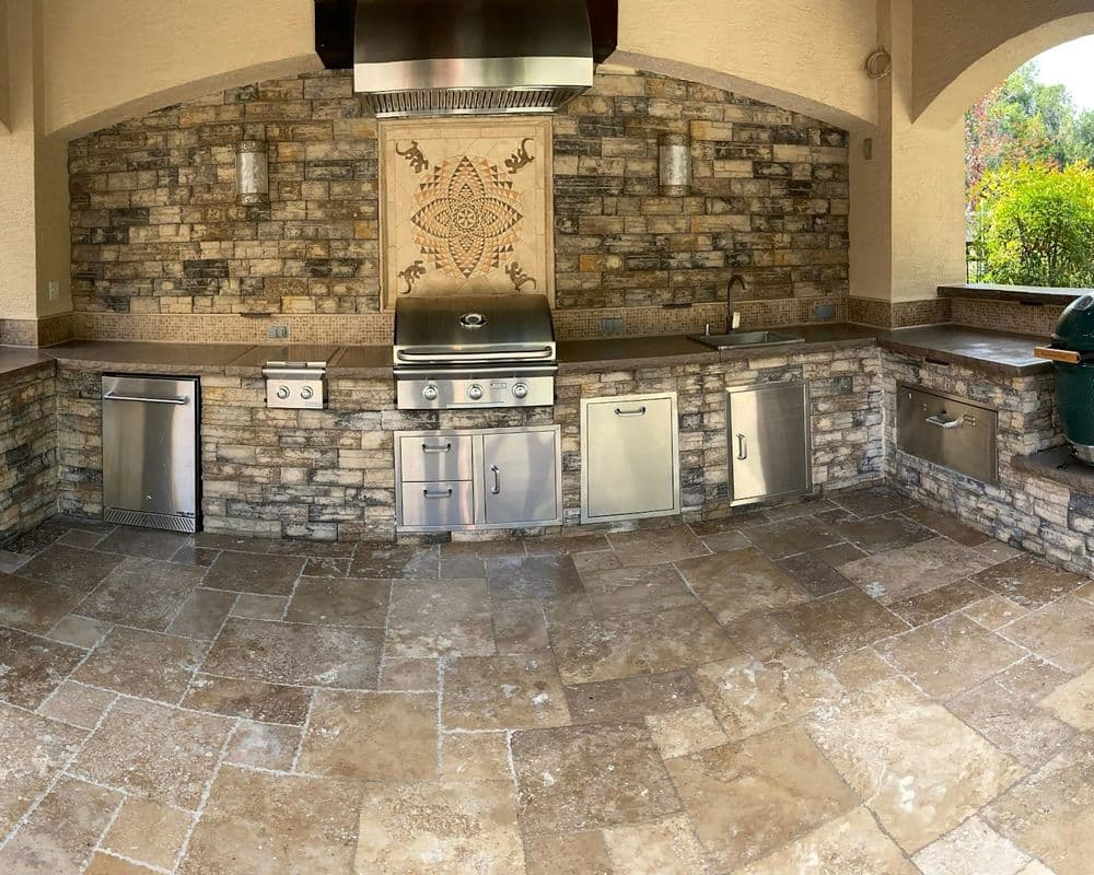 Outdoor kitchen featuring stone walls, stainless steel appliances, and a grill setup.